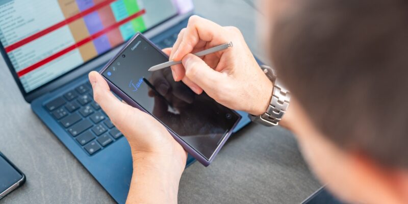 Close up view of man hand holding smart phone and stylus pen at his creative workspace.