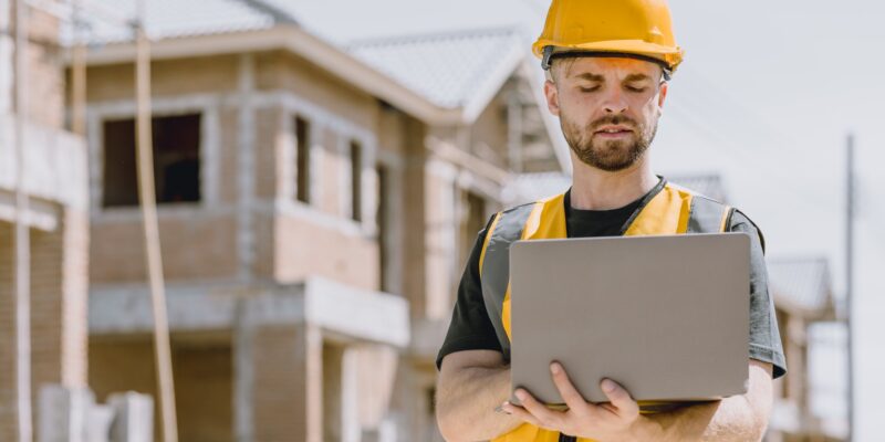 Construction worker Engineer male in safety vest helmet looking laptop computer at construction site