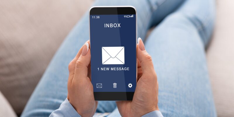Woman Reading E-Mail Message On Smartphone Sitting On Couch Indoor