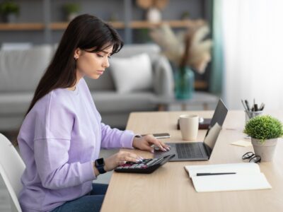 Woman using calculator working on laptop at home